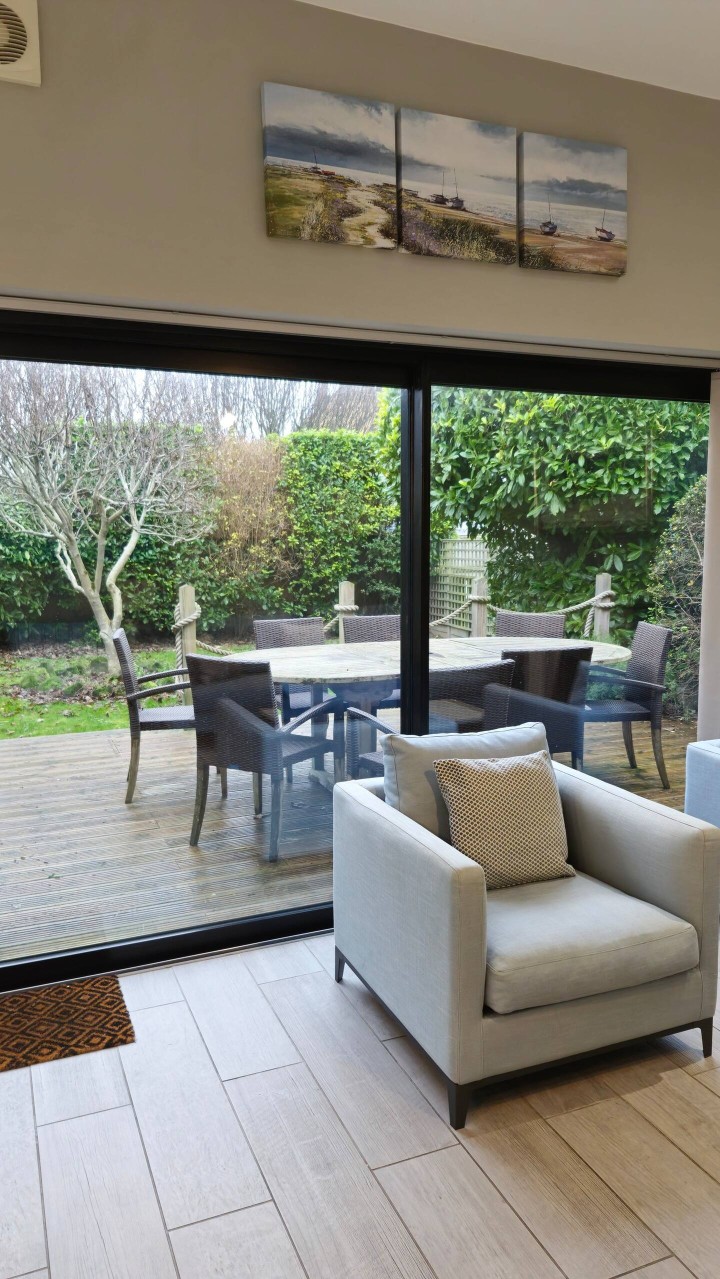 Patio doors leading to garden with seating on decking and BBQ - Devon Cottage
